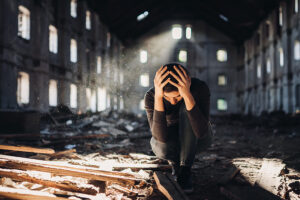 Sad depressed person in abandoned destroyed building crying after natural disaster.